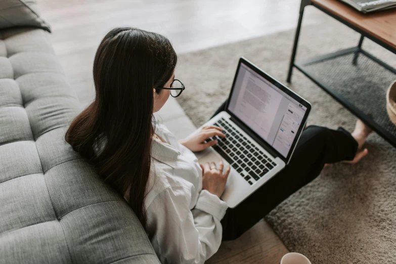 a woman sitting on a couch using a laptop, trending on pexels, wearing black rimmed glasses, bottom angle, office clothes, extremely intricate