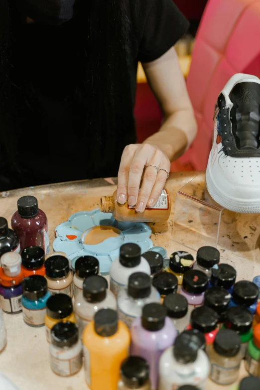 a person sitting at a table with a pair of shoes on it, an airbrush painting, trending on pexels, bottles covered in wax, mid shot, paintchips, “air jordan 1