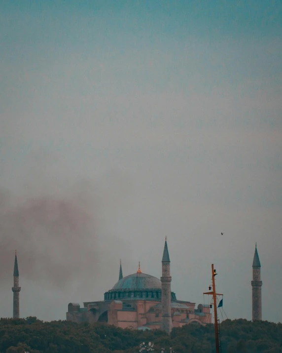 a large building sitting on top of a lush green hillside, a colorized photo, by Ismail Acar, pexels contest winner, hurufiyya, tear gas, minarets, 🚿🗝📝, temples behind her