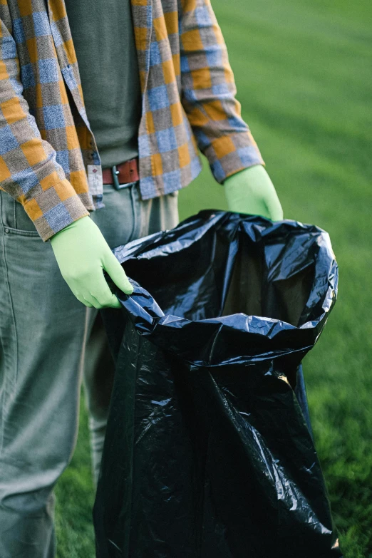 a man standing on top of a lush green field, plasticien, trash can, wearing gloves, black, brown