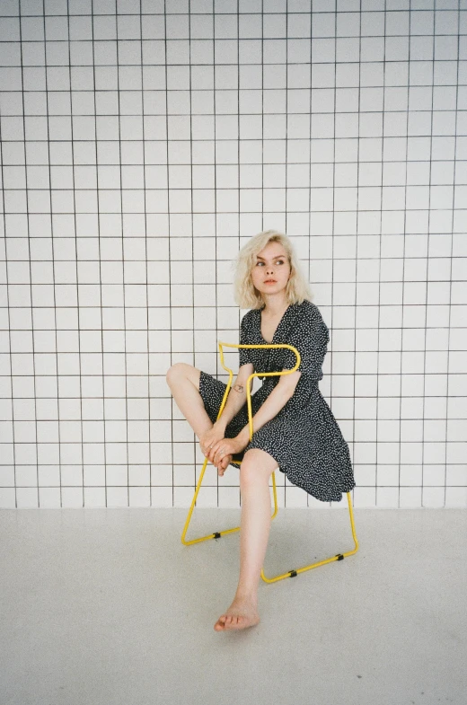 a woman sitting on top of a yellow chair, unsplash, realism, extremely pale blond hair, standing pose, charli bowater, on a checkered floor