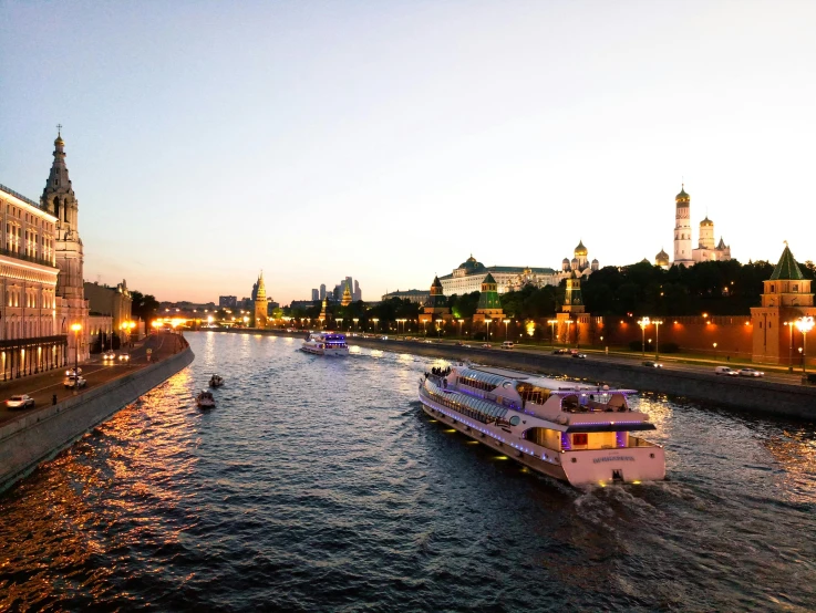 a boat traveling down a river next to a tall building, pexels contest winner, socialist realism, kremlin, twilight ; wide shot, river of wine, vessels