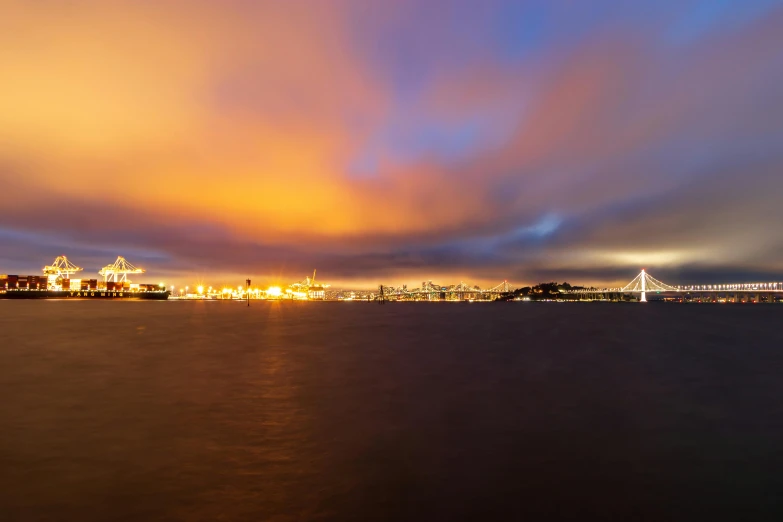 a large body of water with a bridge in the background, by Joseph Severn, unsplash contest winner, city in the distant on fire, panorama, vibrant but dreary gold, port