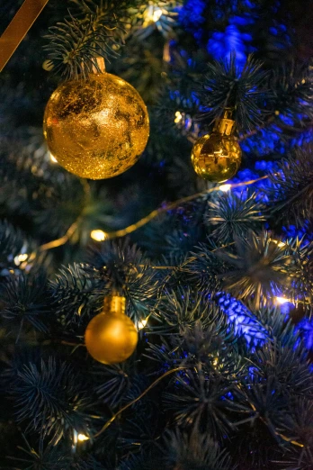 a close up of a christmas tree with ornaments, inspired by Ernest William Christmas, pexels, baroque, blue and yellow lighting, warm coloured, navy, gold