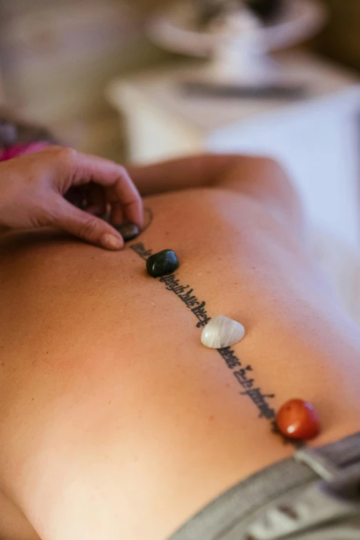 a woman getting a back massage with seven chakrai stones, a tattoo, by Jan Tengnagel, instagram, slate, multi - coloured, mid-shot, brown