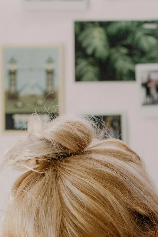 a woman brushing her hair in front of a mirror, poster art, by Rachel Reckitt, trending on pexels, close up of a blonde woman, hair styled in a bun, her hair is natural disheveled, studio photo