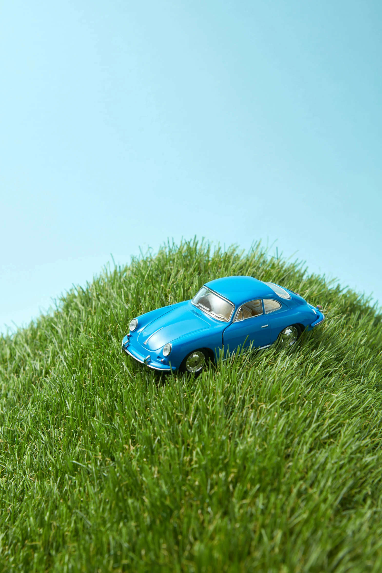 a toy car sitting on top of a lush green field, inspired by Chris LaBrooy, unsplash, photorealism, electric blue, porche, sustainable materials, 1960s color photograph