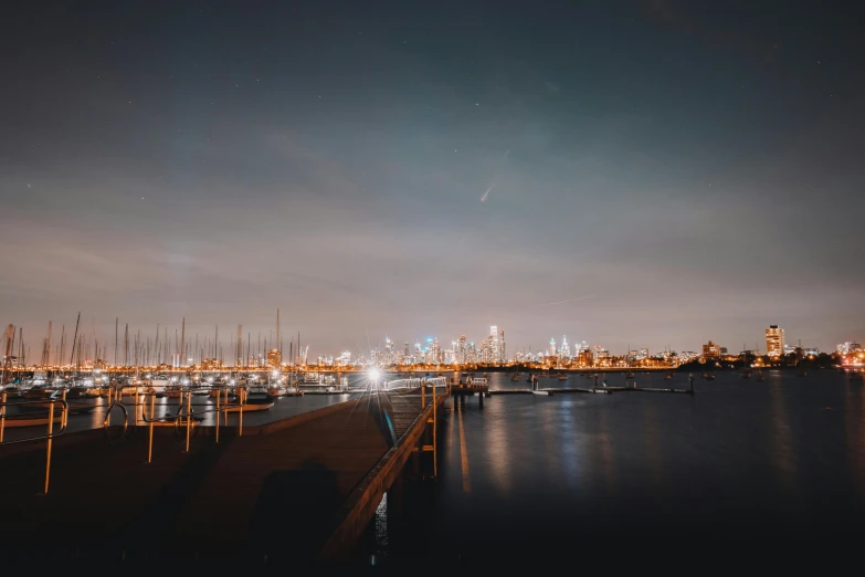 a marina filled with lots of boats at night, pexels contest winner, melbourne, distant cityscape, light beams night, high quality image”