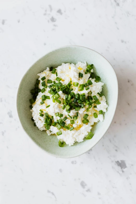 a bowl filled with rice and green onions, inspired by Nishida Shun'ei, sleek white, dwell, mediterranean, cheesy