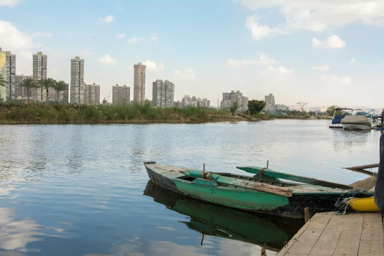 a couple of boats sitting on top of a body of water, by Daniel Lieske, hurufiyya, opposite of urban sprawl, aketan, tech city in the background, near a small lake