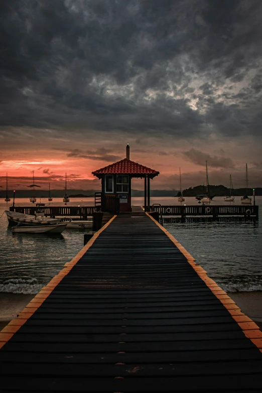 a pier next to a body of water under a cloudy sky, during a sunset, gazebos, ((sunset)), square