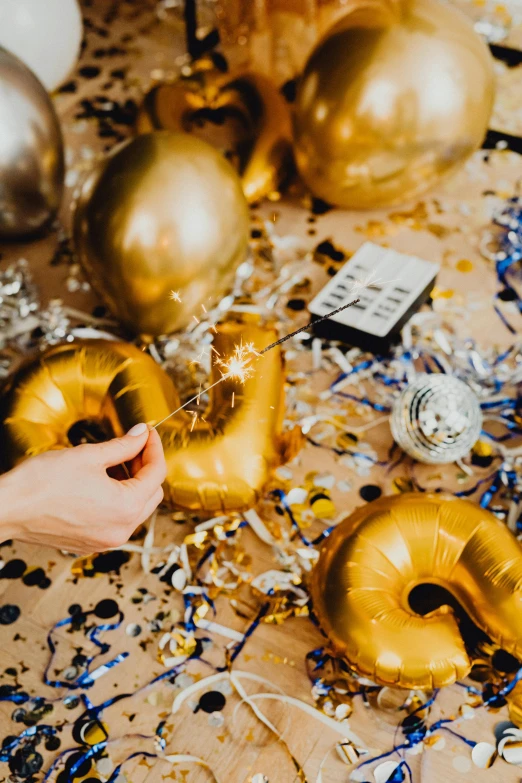 a table topped with gold balloons and confetti, by Julia Pishtar, trending on pexels, process art, hand on table, inflateble shapes, a high angle shot, post graduate