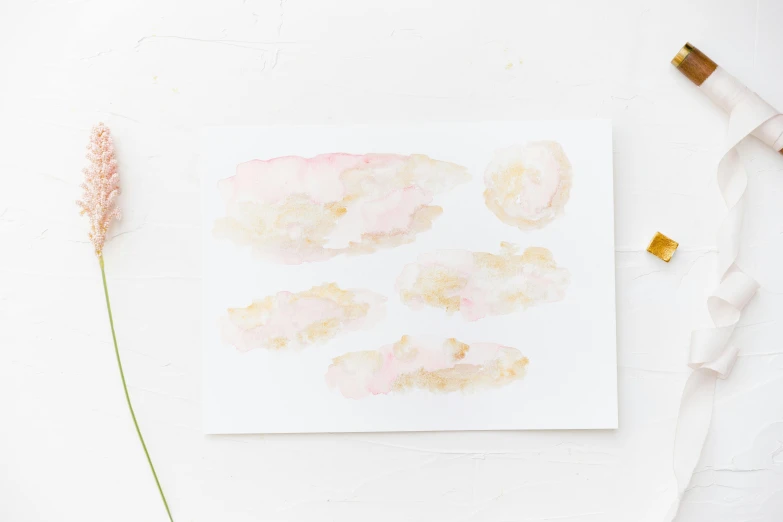 a piece of paper sitting on top of a table, a watercolor painting, light pink clouds, pink and gold color scheme, set against a white background, floating pieces