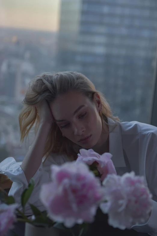 a woman sitting at a table with flowers in front of her, a picture, trending on unsplash, romanticism, movie still of a tired, sydney sweeney, city morning, low quality photo