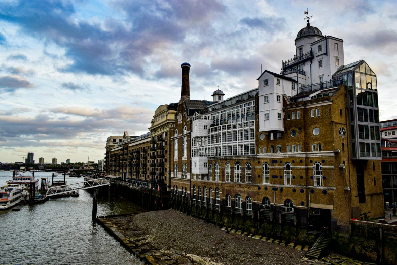 a large building next to a body of water, pexels contest winner, thames river, mills, thumbnail, skies behind