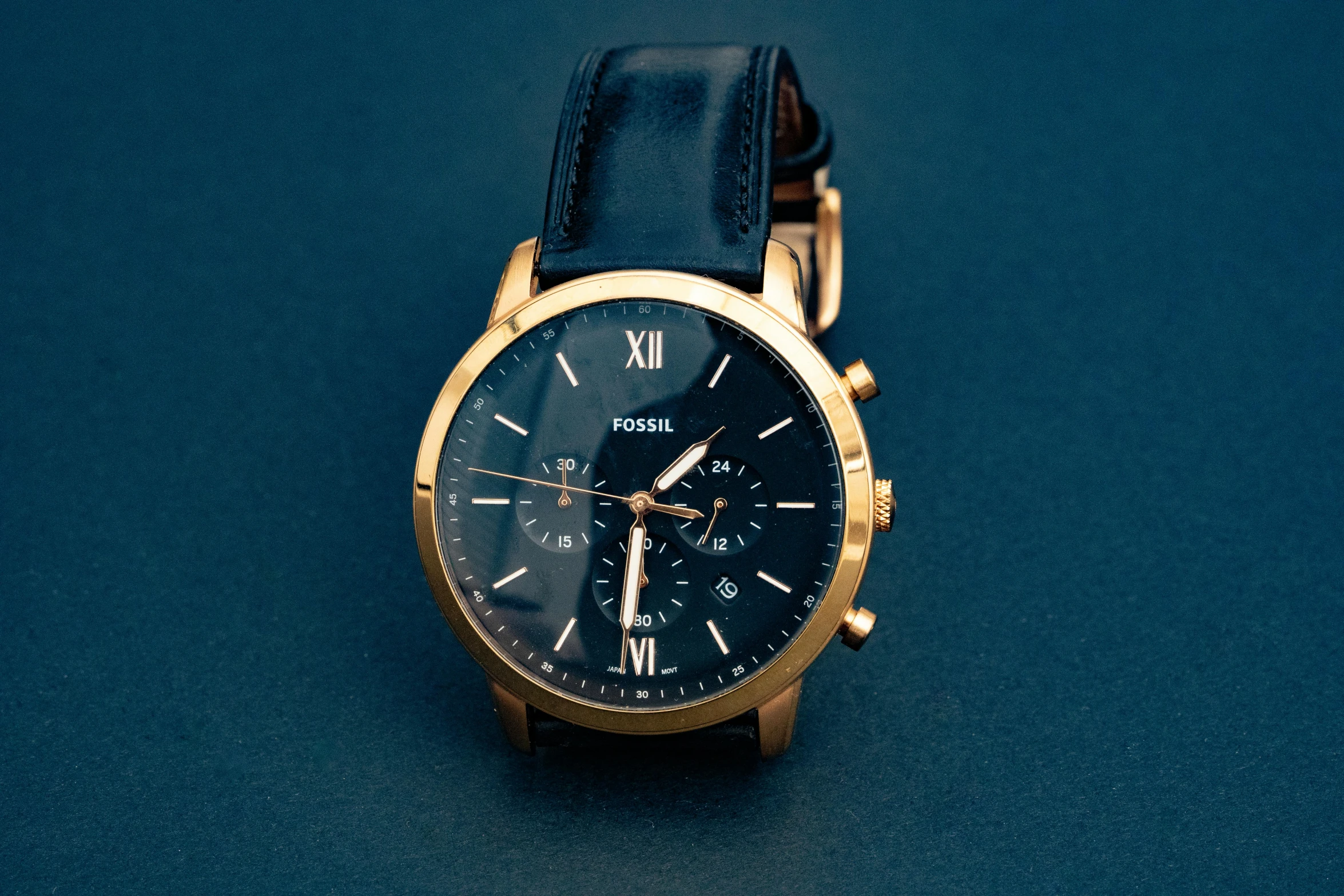 a close up of a watch on a blue surface, a portrait, by Robbie Trevino, unsplash, renaissance, gold and black, fossil, plain background, various posed