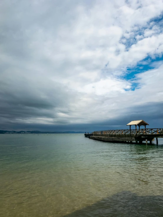 a pier in the middle of the ocean under a cloudy sky, a picture, photograph, wellington, high quality image”