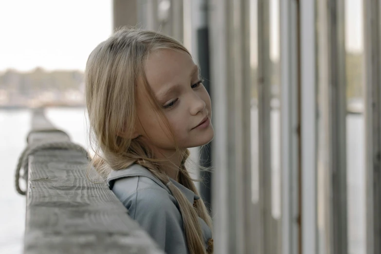 a little girl standing on top of a pier next to a body of water, leaning against the window, 8 k film still, portrait of nordic girl, thoughtful )