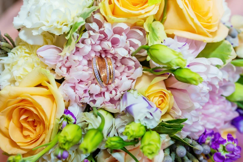 a close up of a bouquet of flowers with two wedding rings, by Anna Findlay, pexels, yellow and purple color scheme, pink and yellow, low detailed, various styles