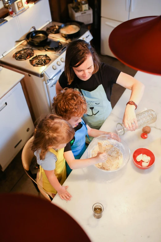 a woman and two children sitting at a kitchen table, by Elizabeth Durack, pexels, baking cookies, high angle shot, profile image, multiple stories