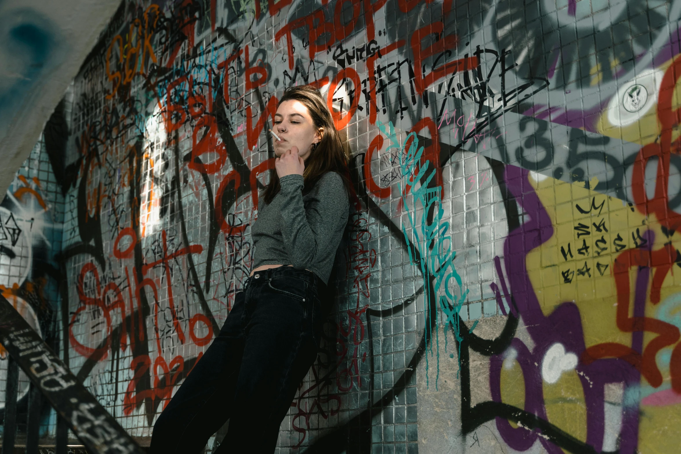 a woman leaning against a wall covered in graffiti, inspired by Elsa Bleda, pexels contest winner, lying down, sydney sweeney, gray skin. grunge, background image