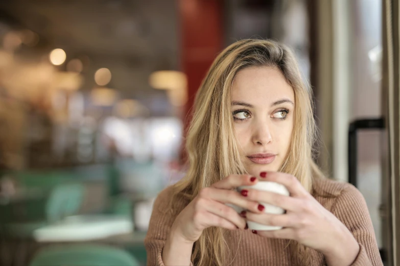 a woman sitting at a table with a cup of coffee, a portrait, trending on pexels, distant expression, mid 2 0's female, handsome girl, multiple stories