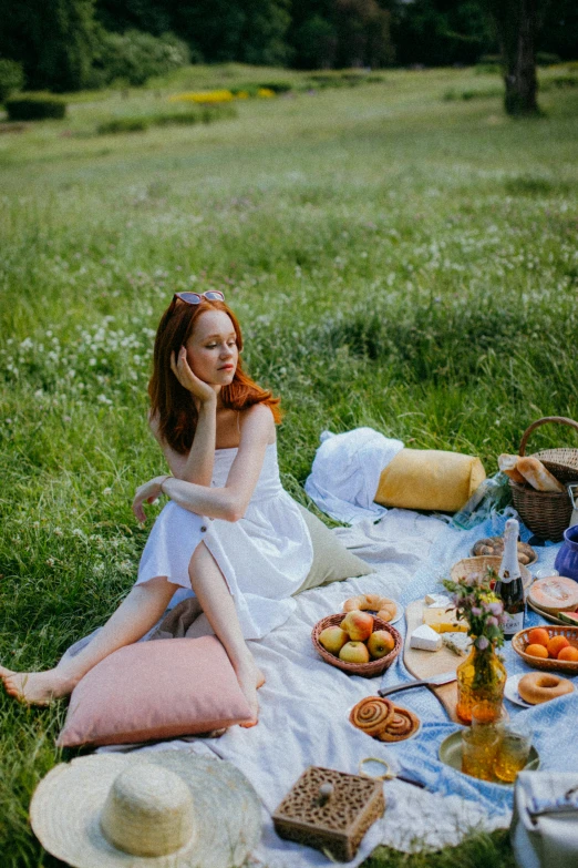 a woman sitting on a blanket in the grass, eating a cheese platter, redhead woman, 2019 trending photo, a beautiful woman in white