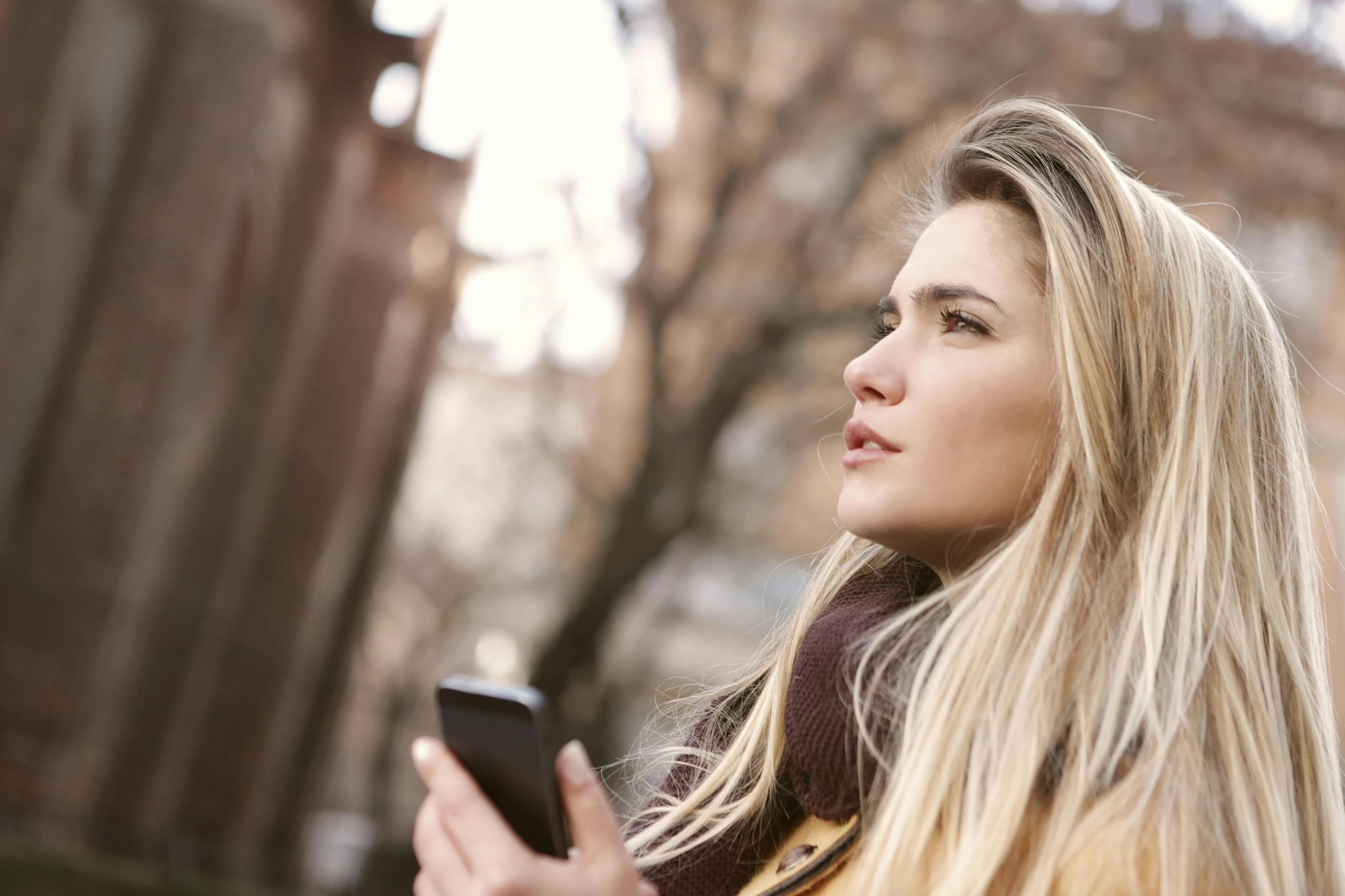 a close up of a person holding a cell phone, trending on pexels, happening, young woman looking up, a girl with blonde hair, warm coloured, pondering