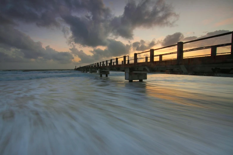 a pier over a body of water under a cloudy sky, a picture, splashing, evening light, andrew dickson, infinite