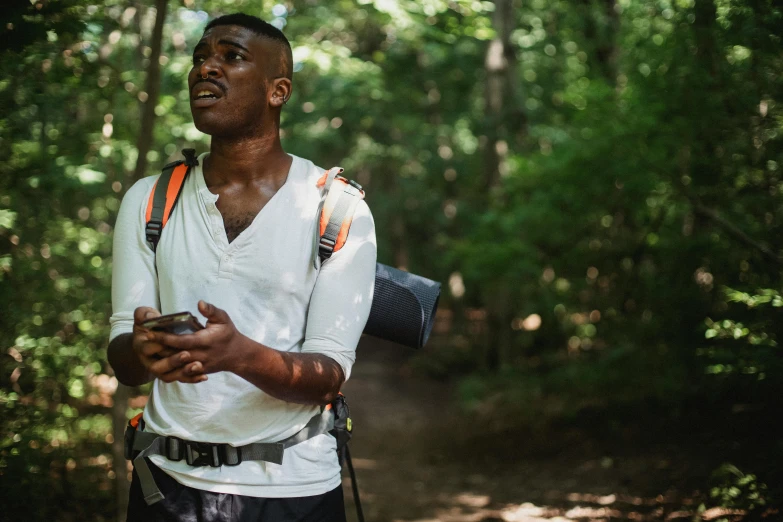 a man standing in the woods holding a cell phone, black man, wearing adventure gear, pilgrimage, profile image