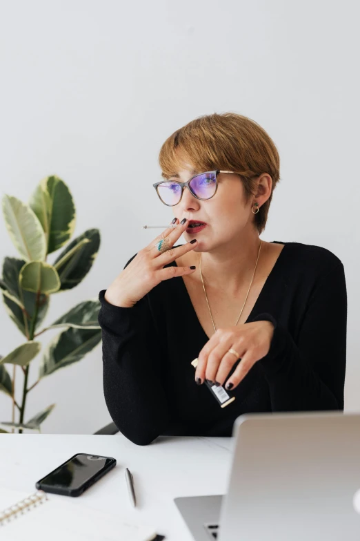 a woman sitting at a desk in front of a laptop, trending on pexels, holding a small vape, pondering, wearing square glasses, professional profile photo