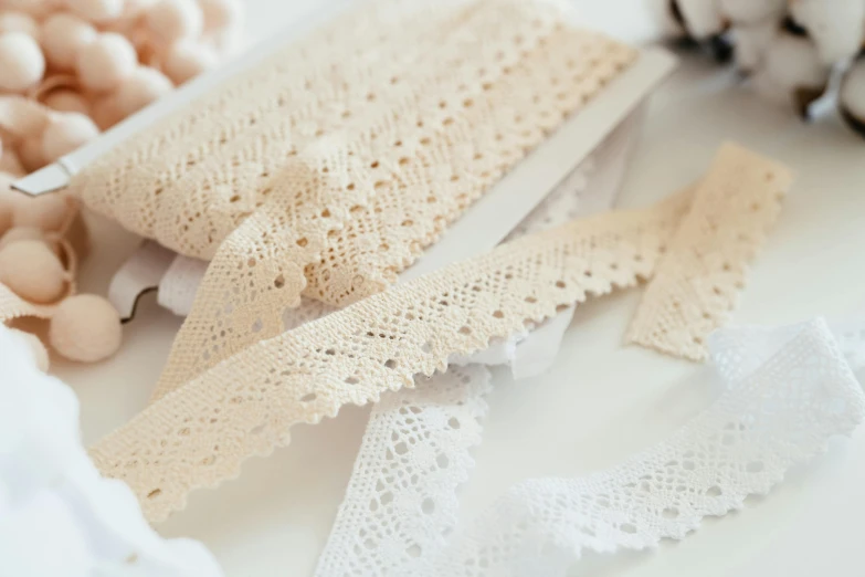 a table topped with lots of different types of lace, unsplash, white ribbon, close-up product photo, beige, trim