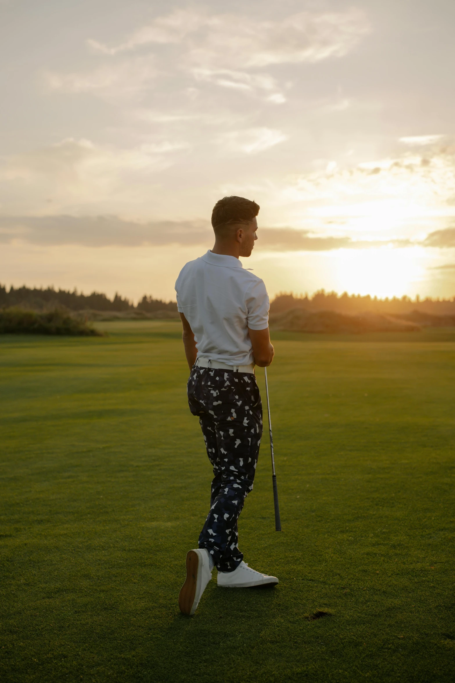 a man standing on top of a lush green field, wearing golf shorts, patterned clothing, sun down, camilo gc