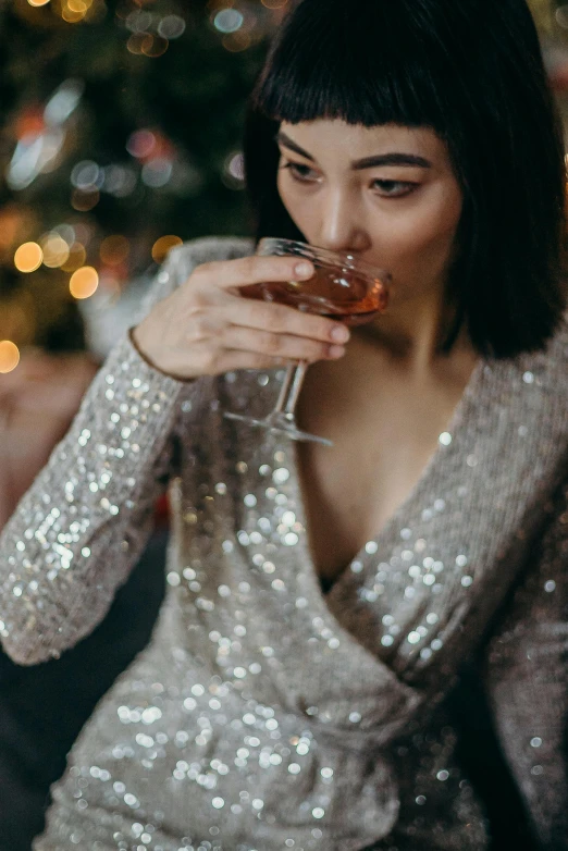 a woman drinking a glass of wine in front of a christmas tree, by Adam Marczyński, trending on pexels, renaissance, wearing silver dress, asian women, sequin top, sitting in a lounge
