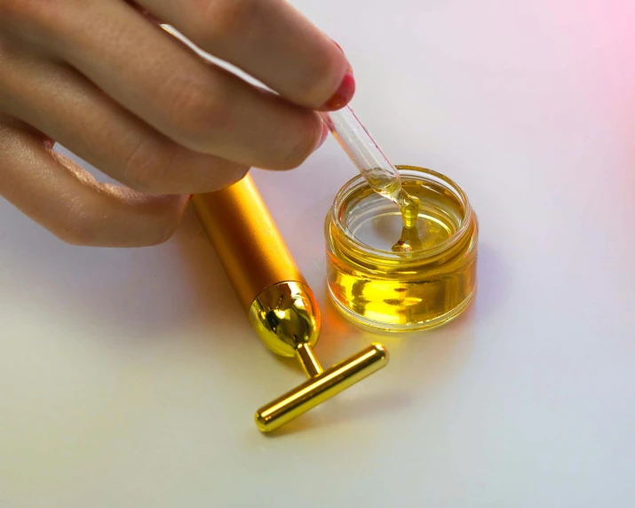 a close up of a person holding a bottle of oil, holding a magic needle, smooth gold skin, product image, syringe