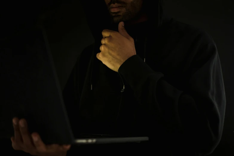 a man in a hoodie using a laptop computer, unsplash, computer art, dressed in black body armour, ( ( dark skin ) ), black, stealth