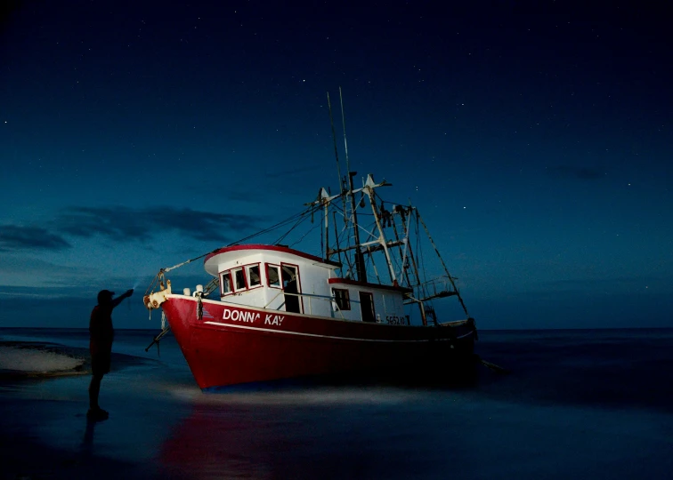 a man standing next to a boat on a beach, by Doug Wildey, pixabay contest winner, art photography, night time footage, crimson tide, fishing boat, photo taken from a boat