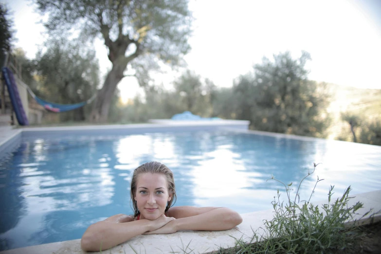 a woman sitting at the edge of a swimming pool, a portrait, unsplash, olive trees, portrait image