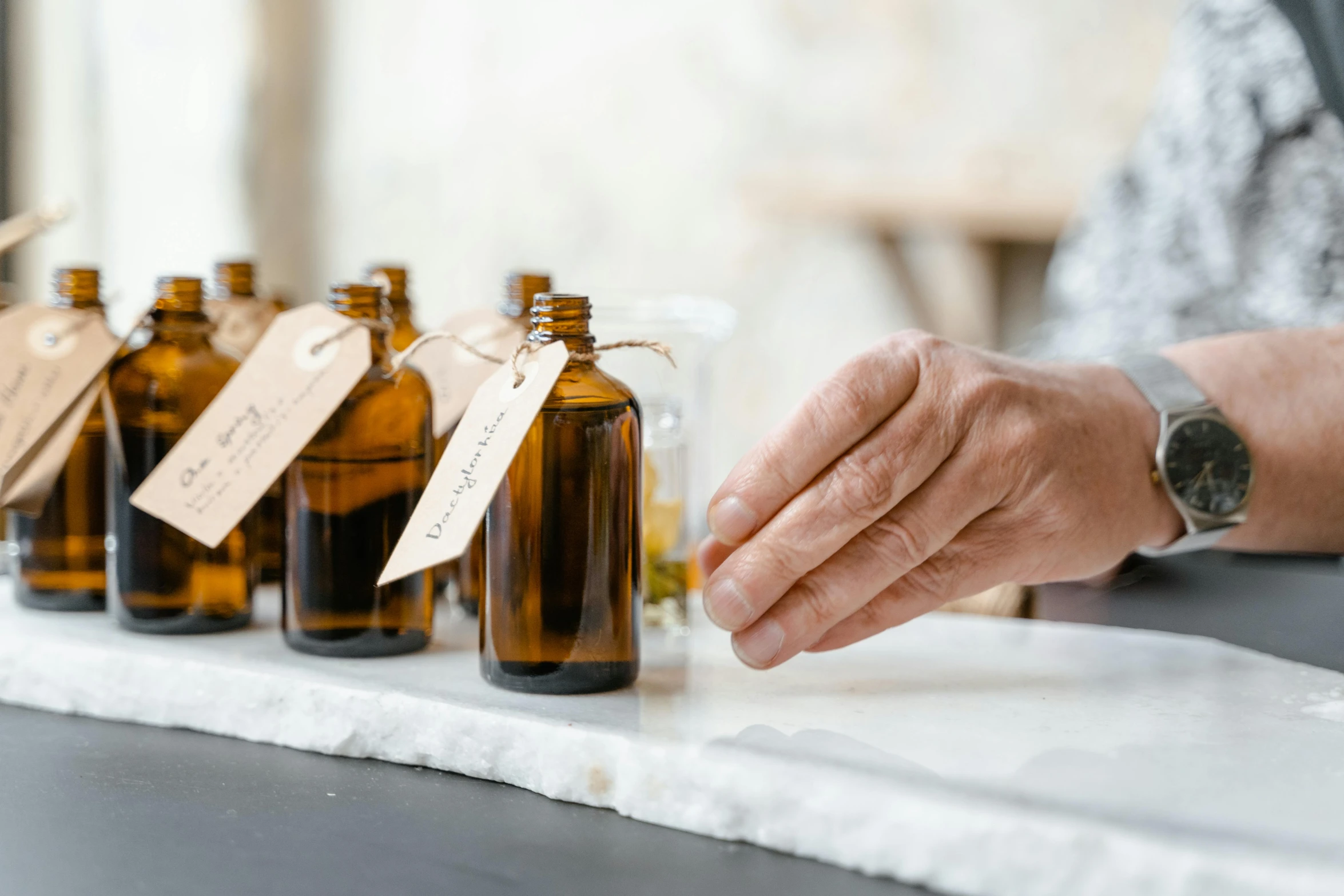 a close up of a person placing small bottles on a table, by Helen Stevenson, unsplash, beautiful labels, natural materials, amber, set against a white background