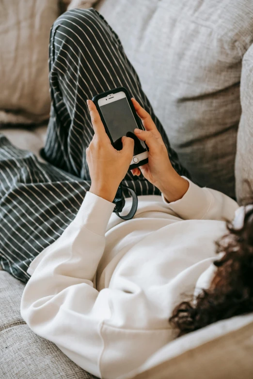 a woman laying on a couch using a cell phone, trending on pexels, wearing pajamas, grey, smart textiles, gen z