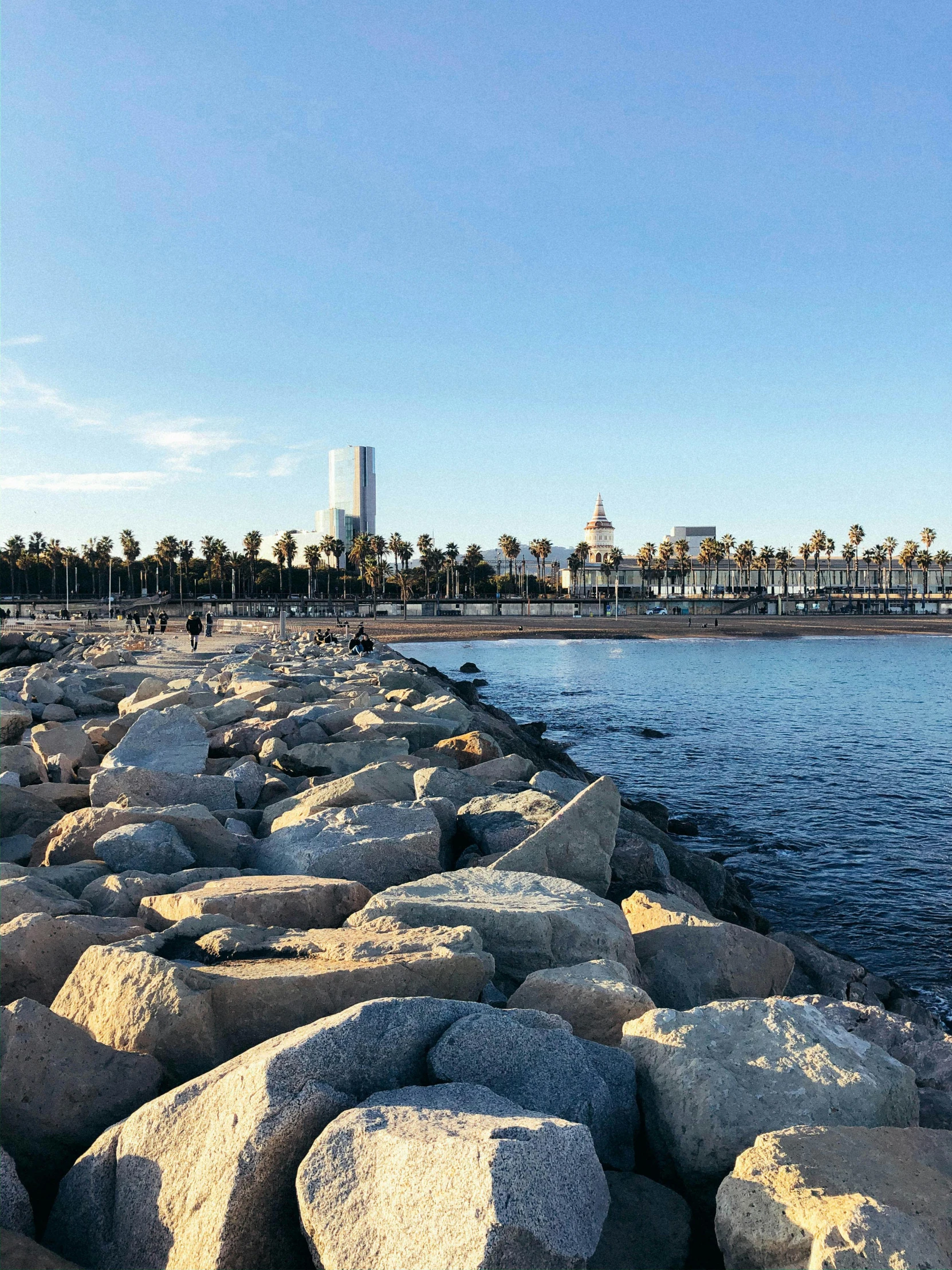 a group of large rocks sitting next to a body of water, happening, barcelona, long beach background, profile image, multiple stories