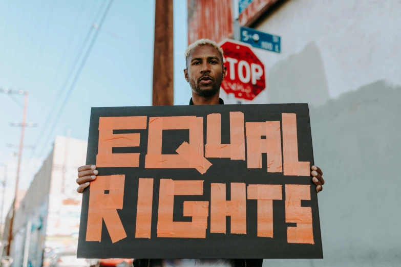 a man holding a sign that says equal rights, by Julia Pishtar, trending on pexels, black arts movement, frank ocean, profile image, coloured photo, 1 2 9 7
