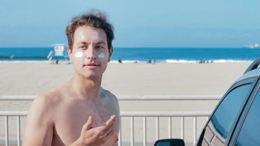 a man standing next to a car on a beach, white face paint, skincare, paulie shore, putting makeup on