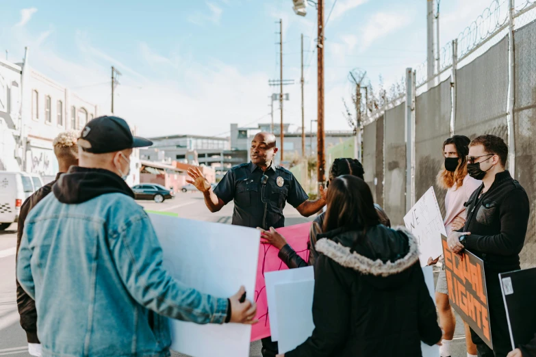 a group of people standing on the side of a road, graffiti, teaching, panel of black, police officers, influencer