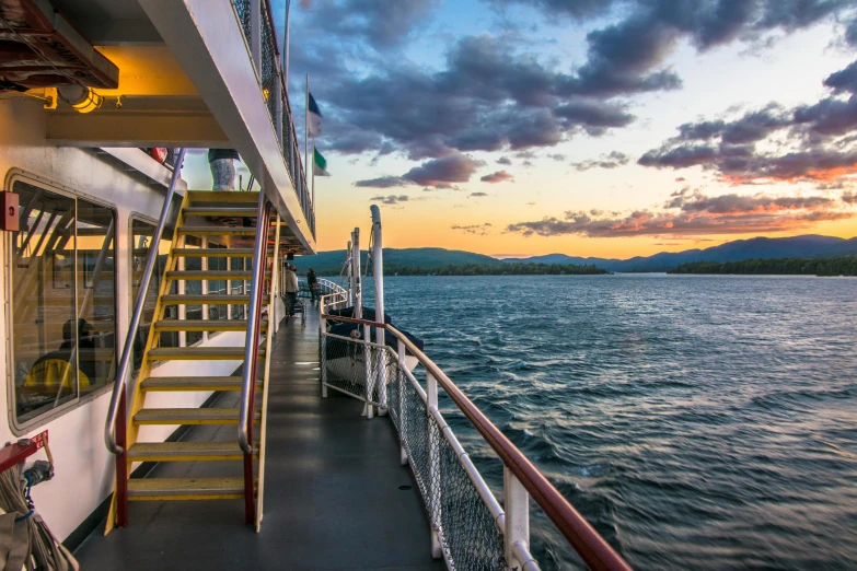 a boat on a body of water with mountains in the background, the deck of many things, in the evening, on ship, travel guide