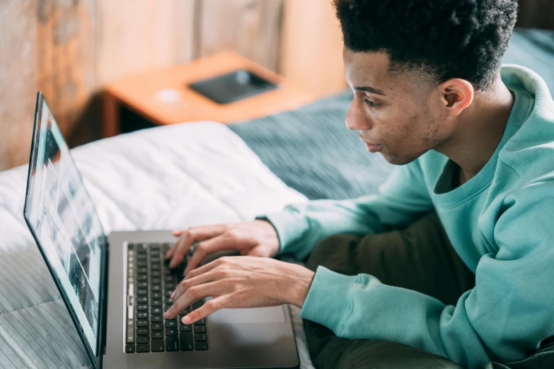 a man sitting on a bed using a laptop computer, a screenshot, by Carey Morris, trending on pexels, black teenage boy, concentration, from waist up, educational