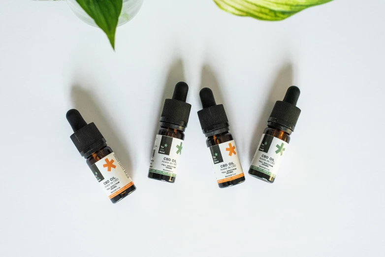 three bottles of cbd oil next to a plant, a portrait, by Emma Andijewska, trending on pexels, green and orange theme, high view, front facing, the stars