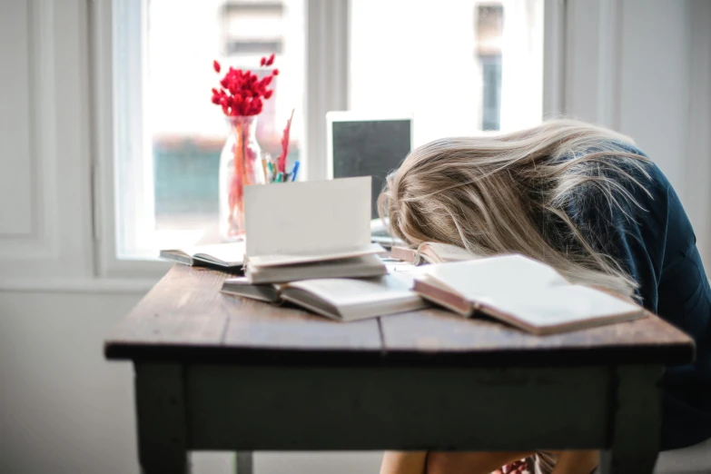 a woman sitting at a desk with her head in her hands, by Alice Mason, pexels, sleeping, post graduate, run down, on a table