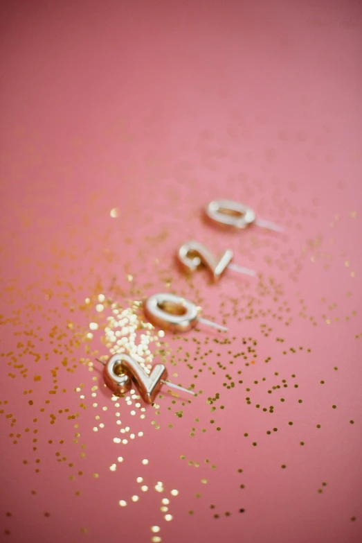 the word love spelled in gold glitter on a pink background, by Julia Pishtar, happening, graduation photo, studs, '20, white candles