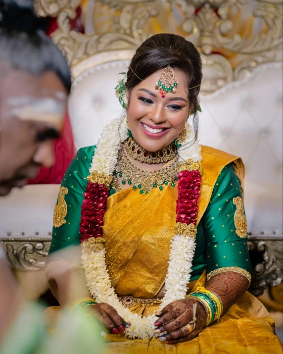 a woman sitting on top of a couch next to a man, pexels contest winner, hurufiyya, wearing elaborate green and gold, hindu, she is smiling, bride